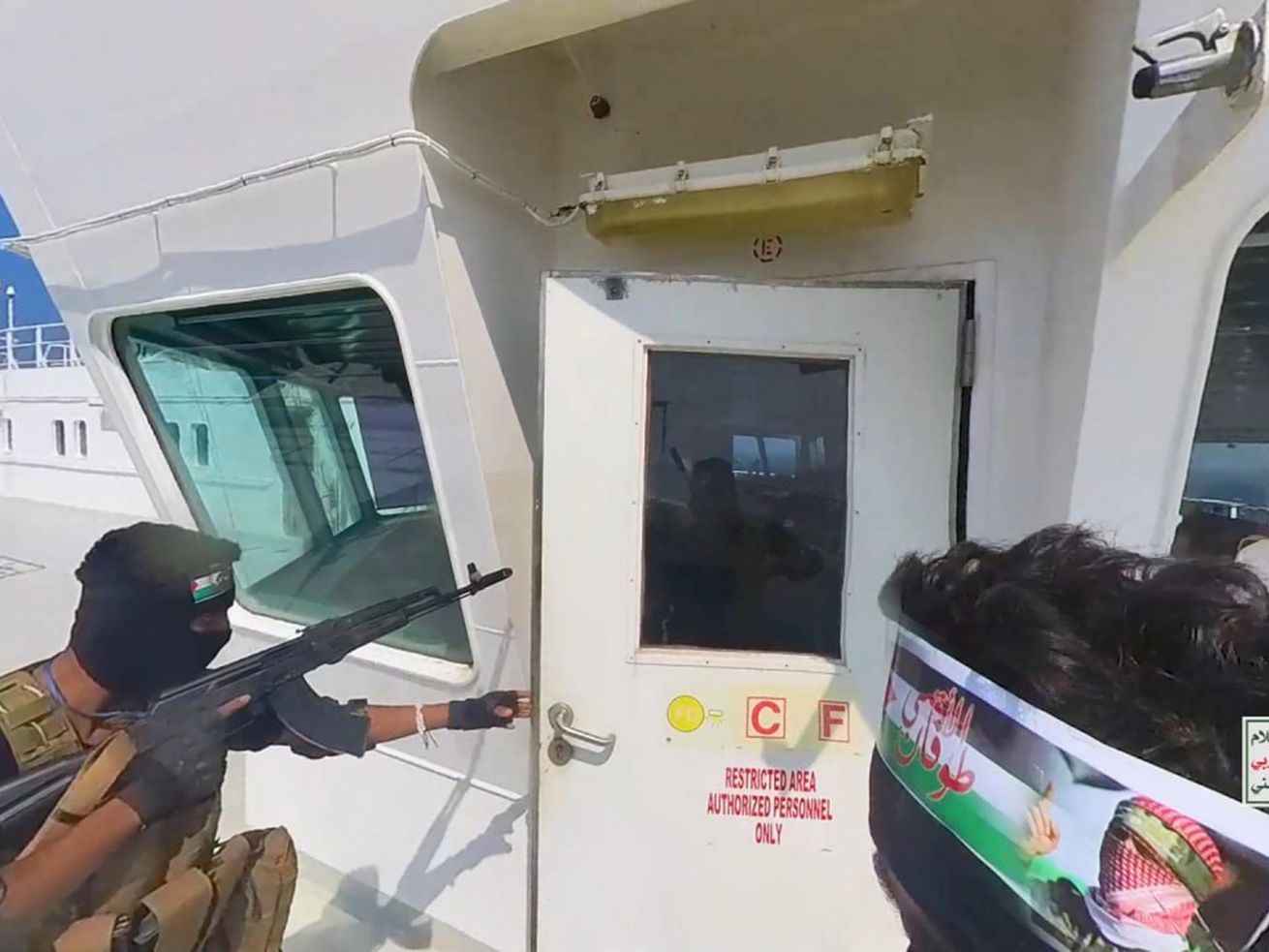 An armed man opens a door on the deck of a cargo ship.