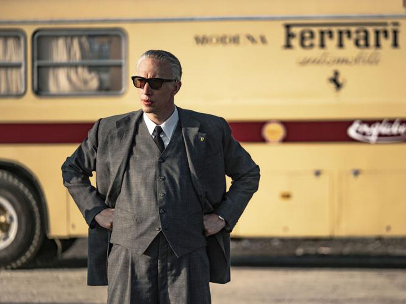 A man with white hair and sunglasses in a natty suit in front of a trailer that says “Ferrari” on the side