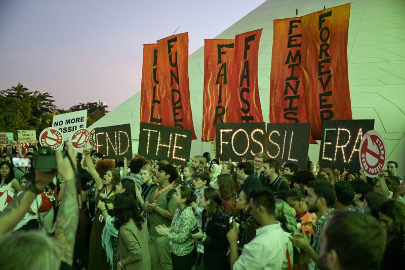 People hold signs reading “End The Fossil Era” during a protest.