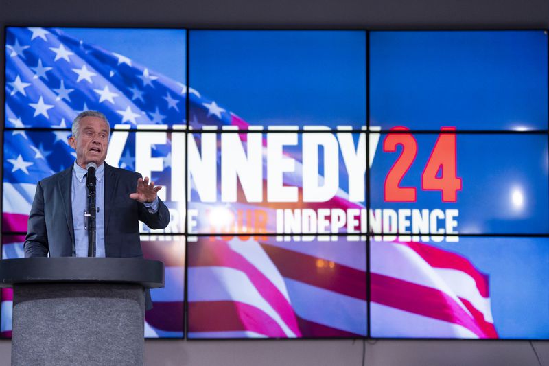 Robert F. Kennedy speaks at a lectern with video screens showing his campaign slogan in the background.