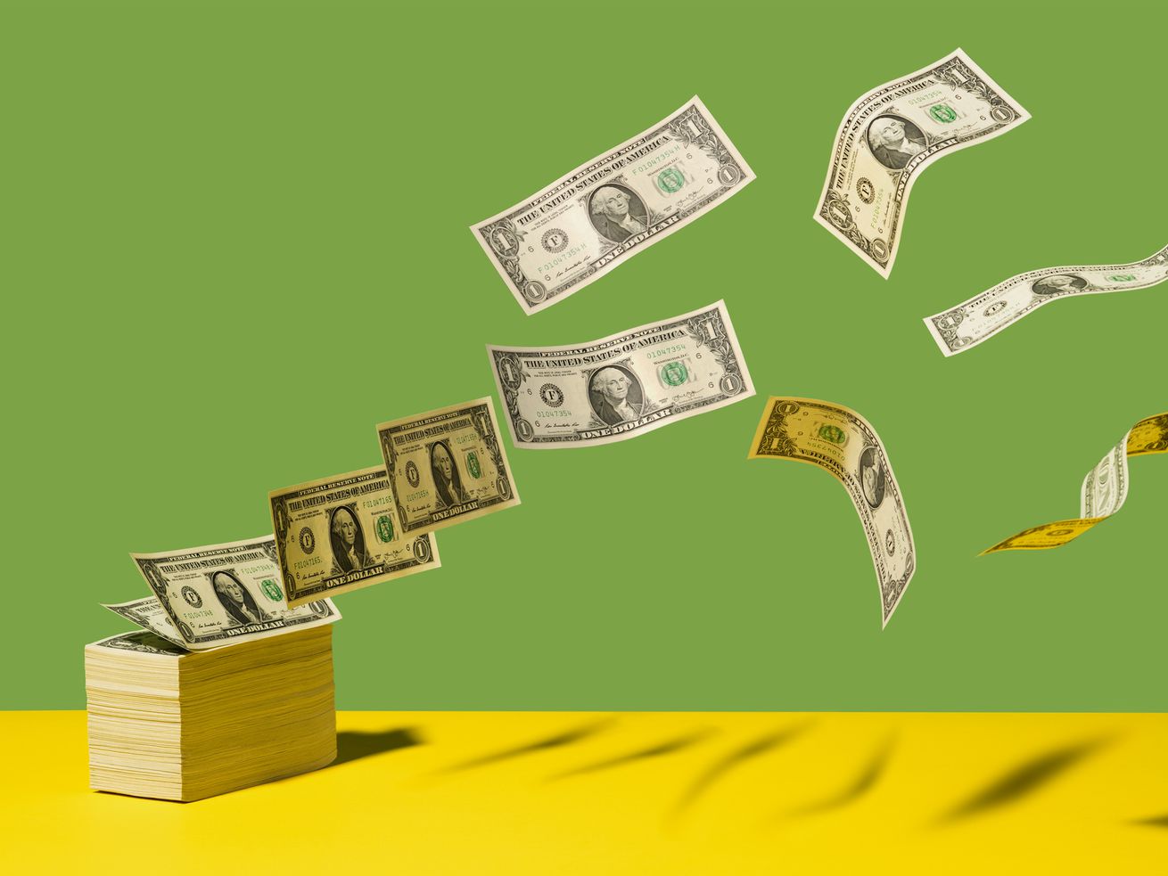 Stack of US $1 bills with bills flying away on yellow shelf, green background.