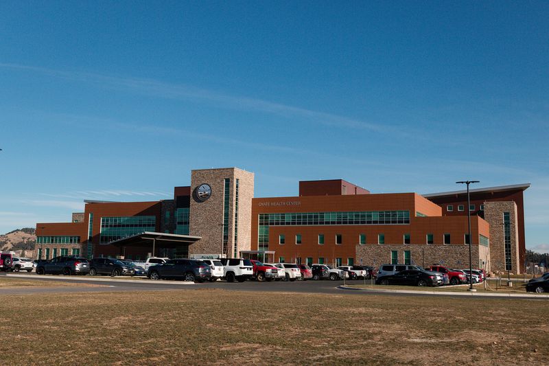 Exterior view of a large red-and-tan brick medical complex against a blue sky.