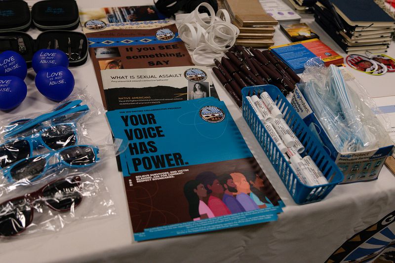 Promotional items including pens, lip balms, sunglasses, and pamplets reading “Your voice has power,” and “What is sexual assault.”