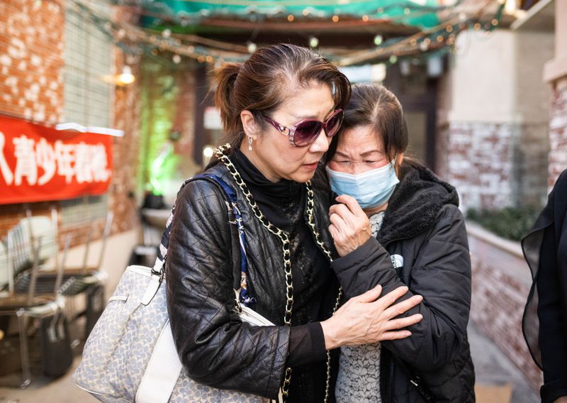 Two older Asian women stand comforting each other.