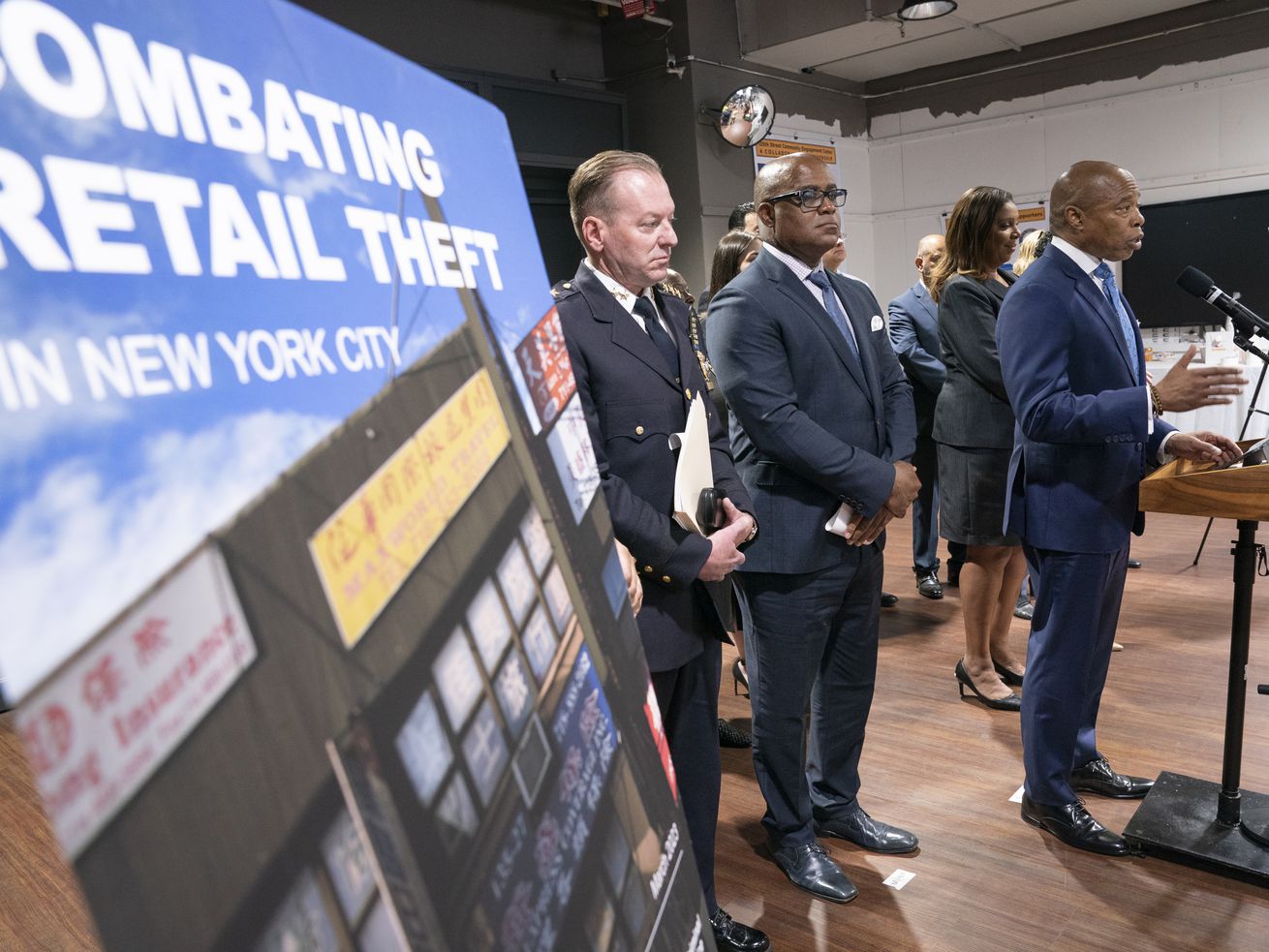 Sigh that reads “Combating Retail Theft” is seen in the foreground while New York City Mayor Eric Adams speaks at a lectern.