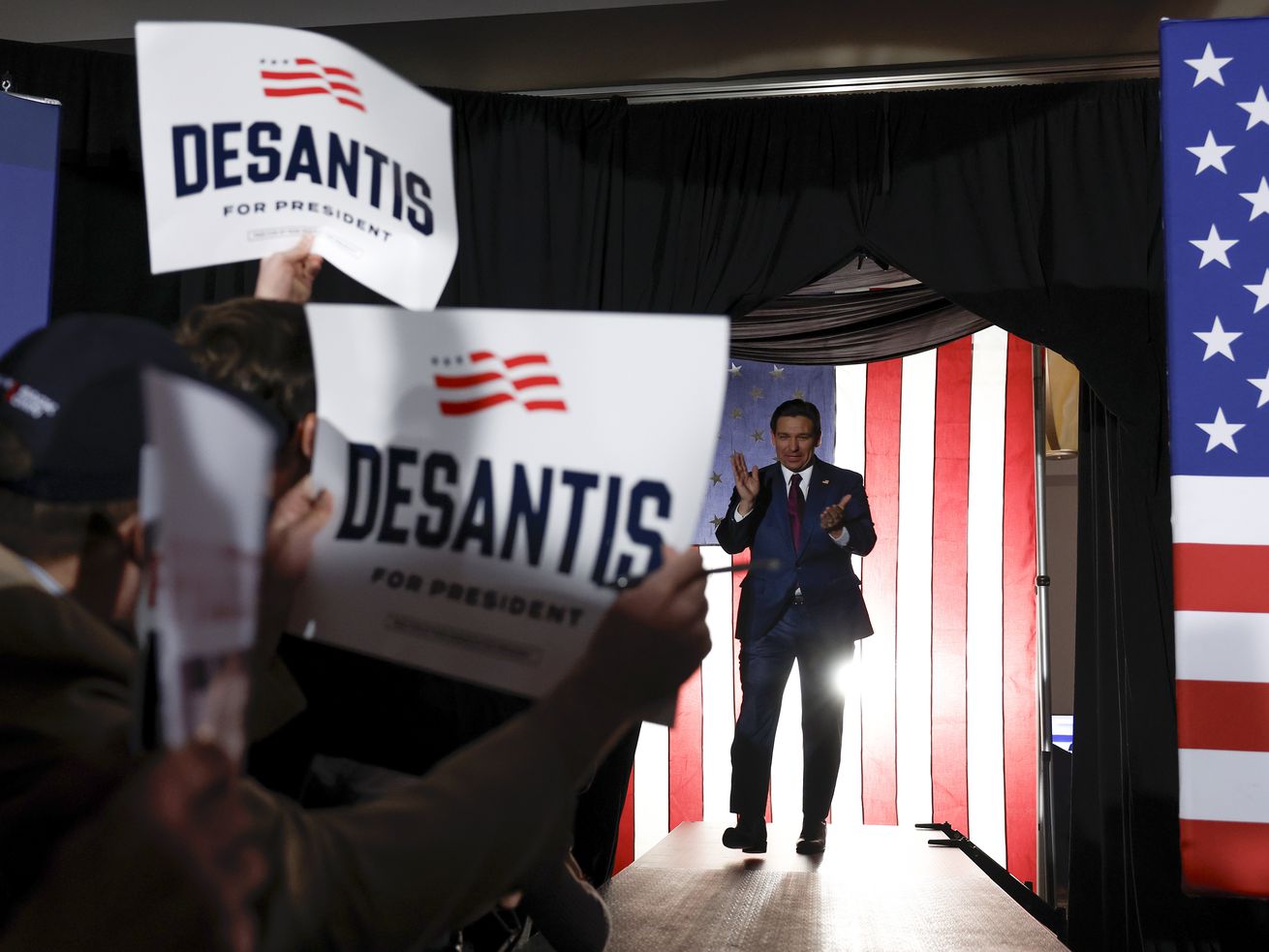 People wave DeSantis signs as Florida Gov. Ron DeSantis enters the room.