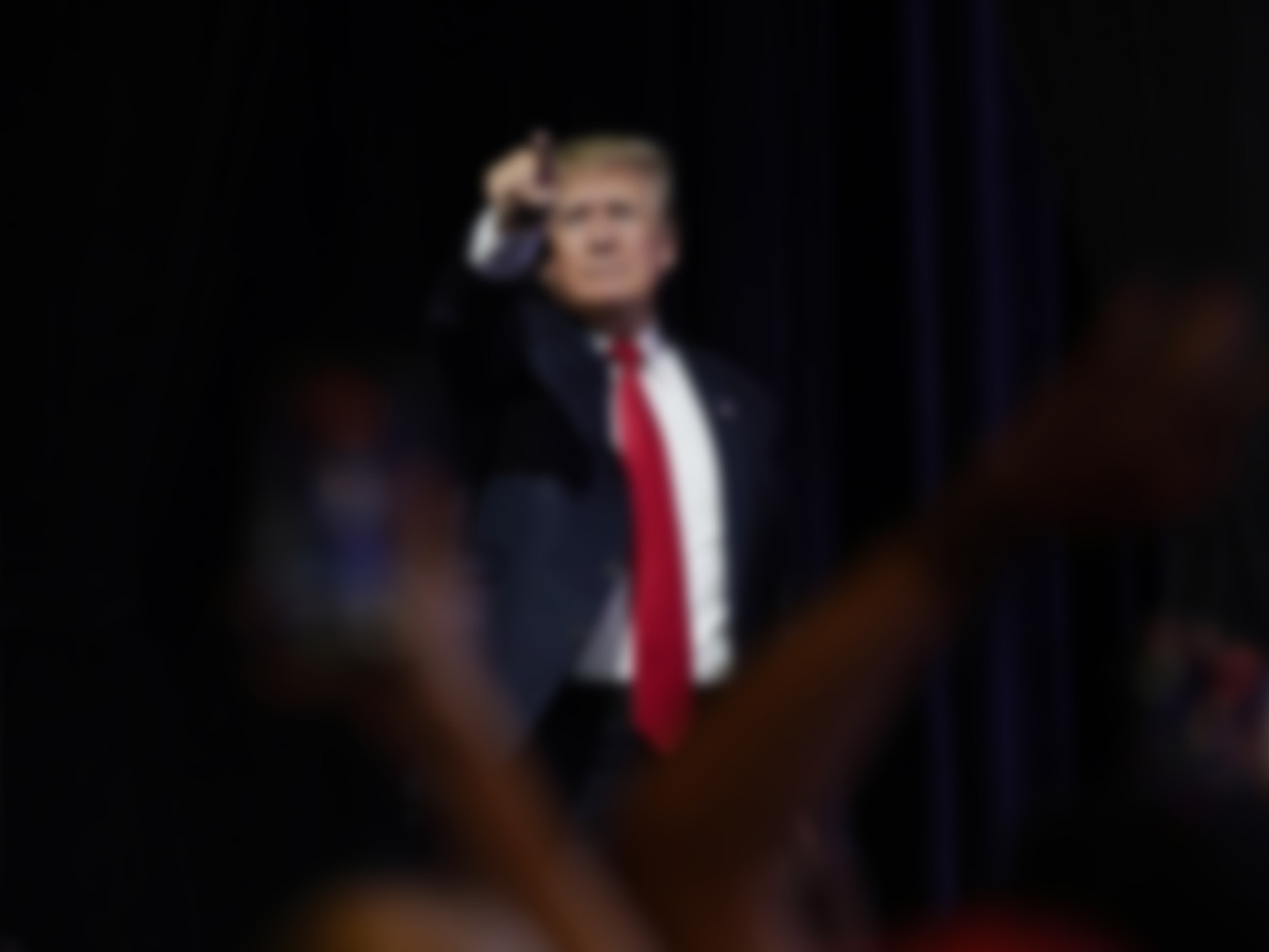 A blurry photo of Trump pointing out at a crowd from a stage.