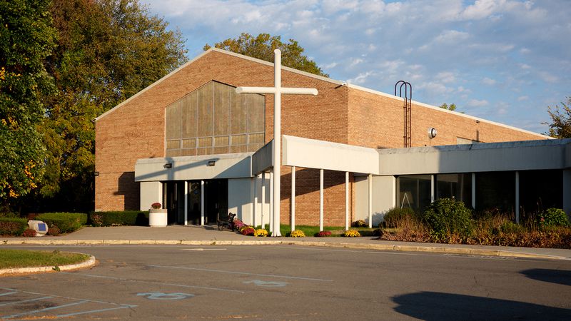 A large red brick building with a white cross and a parking lot.