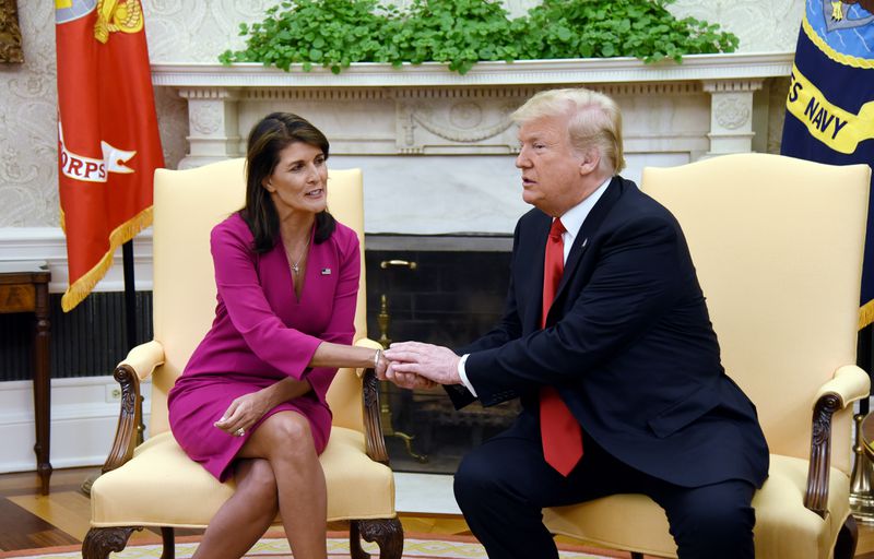Haley and Trump sit, Trump holding one of Haley’s hands with both of his. 