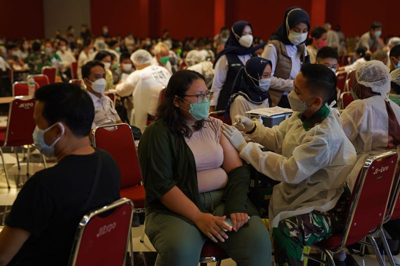 A person receives a vaccine shot in a room full of masked people.