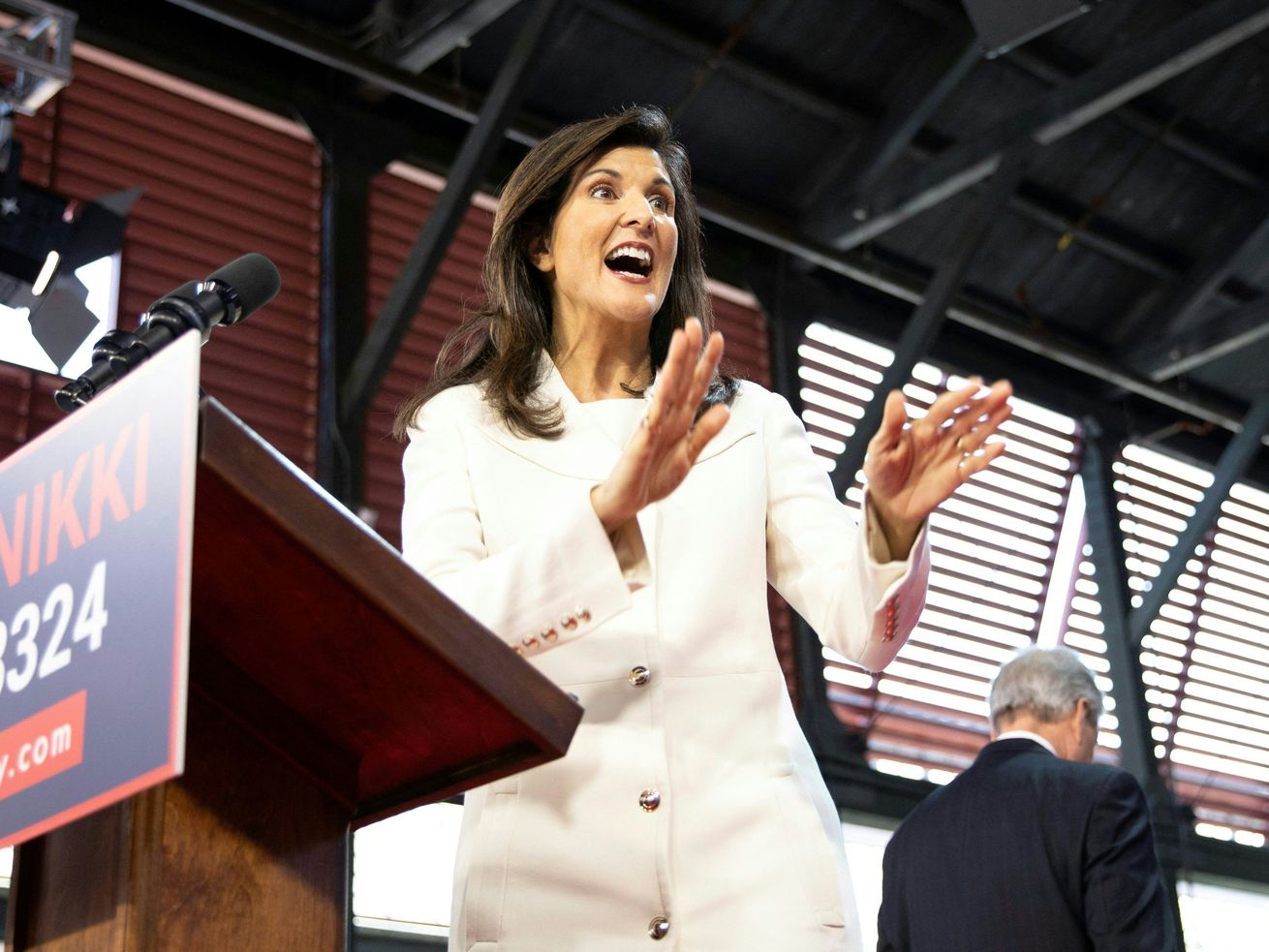 Nikki Haley gestures to someone off camera, standing in front of a lectern. 