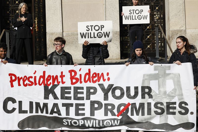 Several young people hold a giant banner which reads “President Biden: Keep Your Climate Promises.” Smaller signs in the background read “Stop Willow.”
