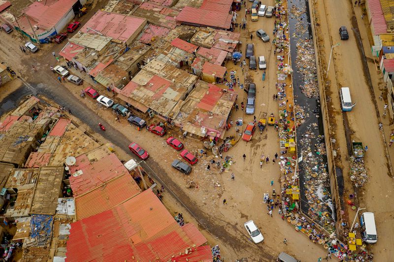 Luanda City street markets in Angola pictured from above. Dirt roads are hemmed in by metal roofs, and the streets are lined with cars.