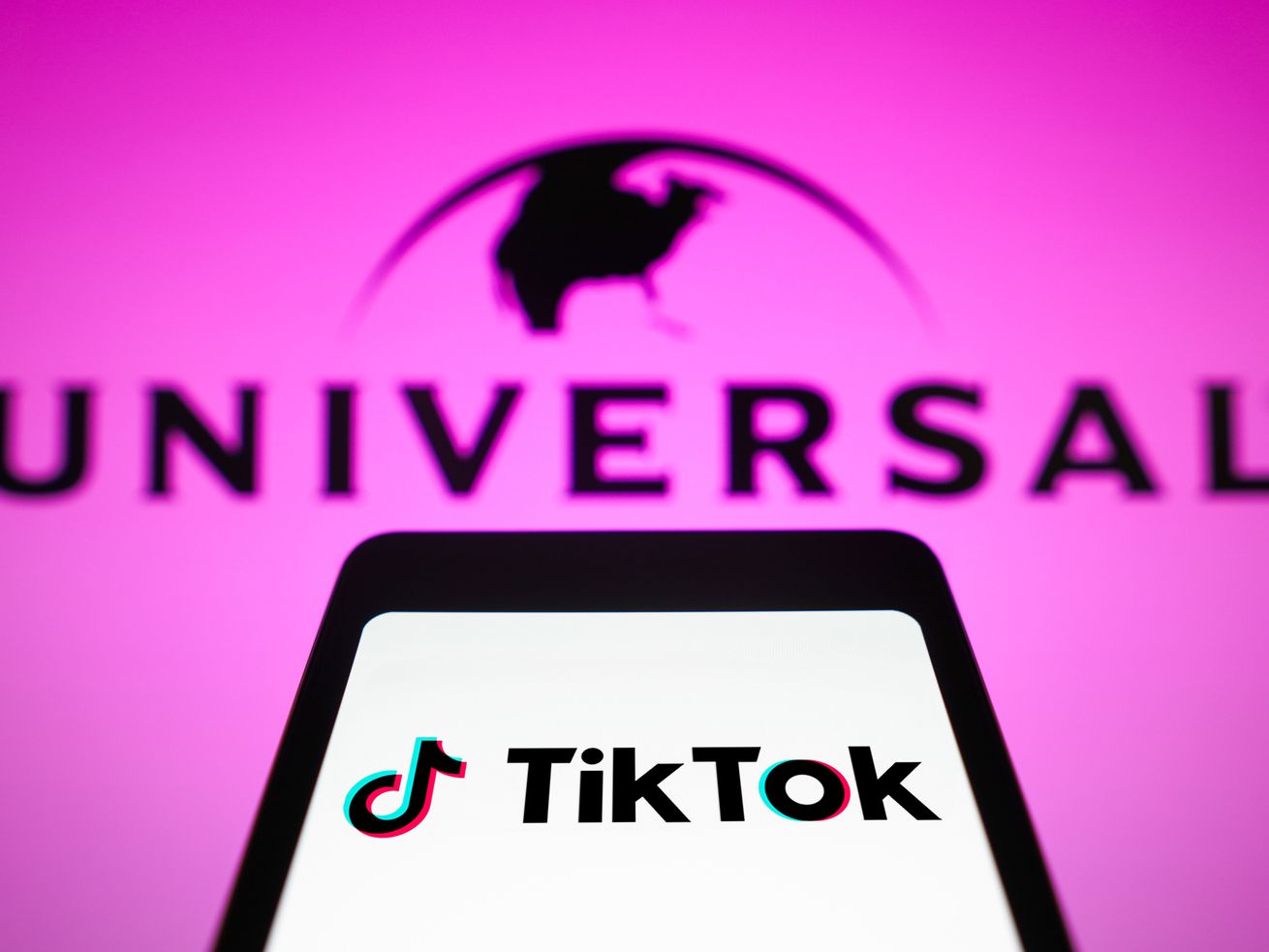 In this photo illustration, the TikTok logo is displayed on a&nbsp;smartphone screen with the logo for Universal Music in the background.&nbsp;