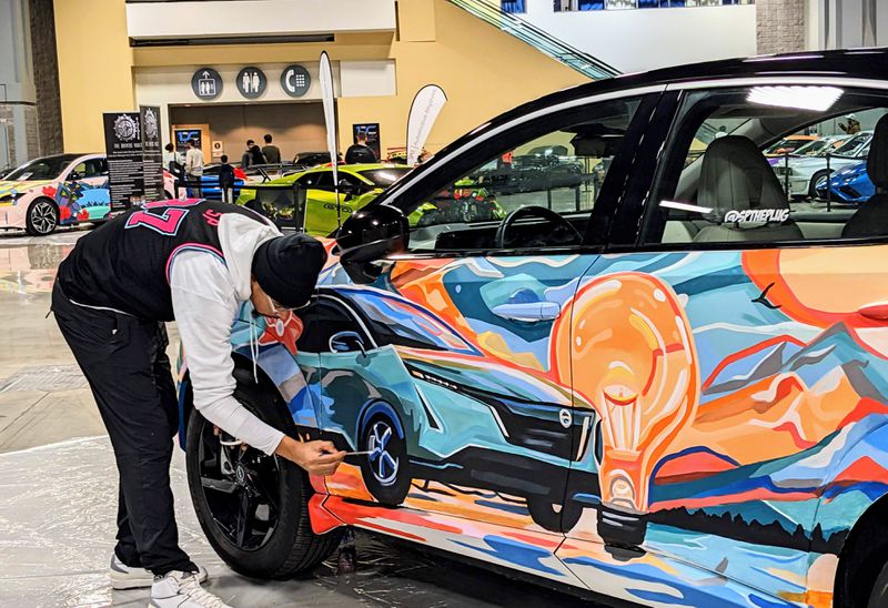 An artist paints images of a car, a lightbulb, and a mountain scene on an electric SUV.